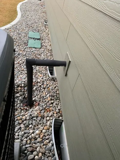 Black metal pipe attached to a house wall over rocky ground. Black metal pipe attached to a house wall over rocky ground.